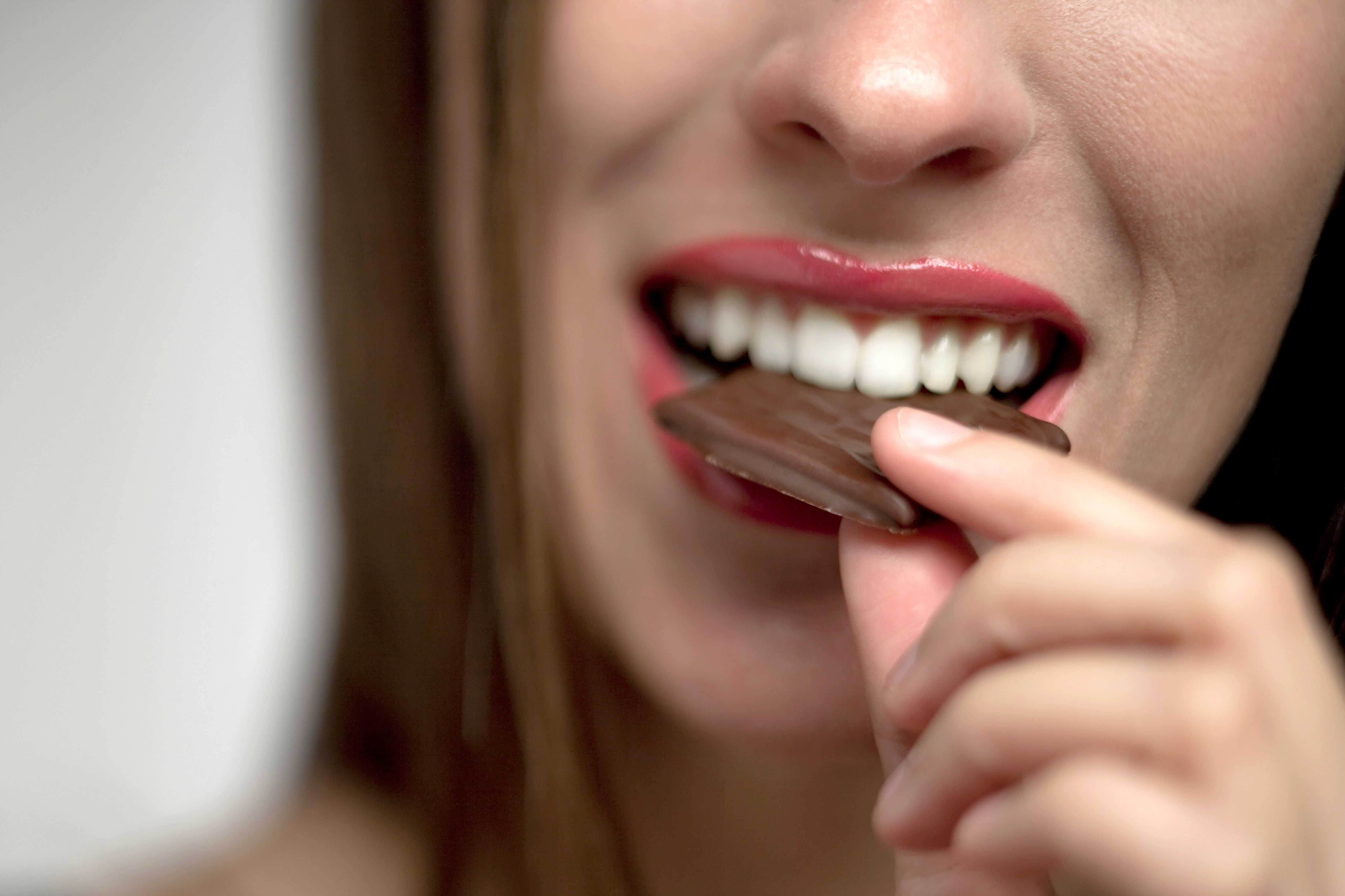 woman bites into a piece of chocolate candy